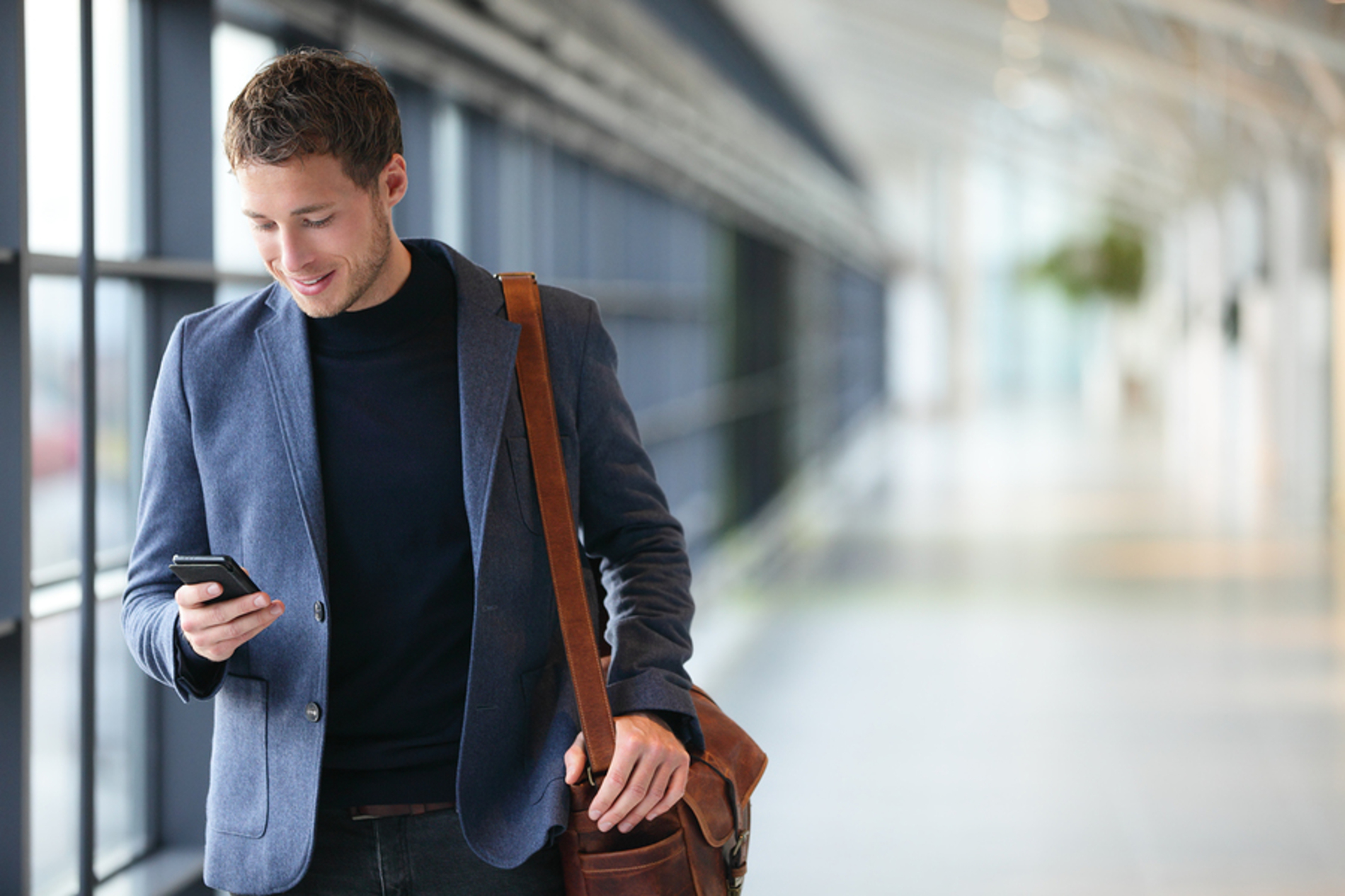 Man walking down a hallway while looking at his phone.