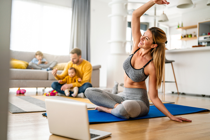 Woman sitting on the floor stretching in front of her laptop.