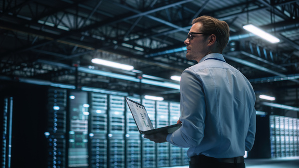 Standing in a server room holding a laptop.