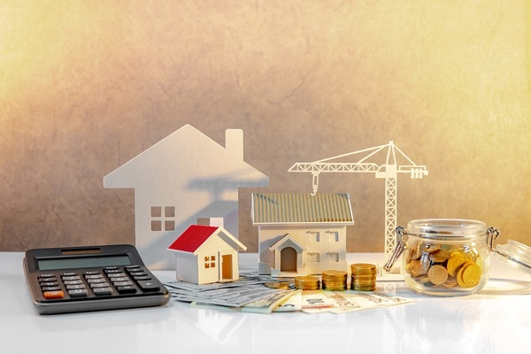 Calculator, glass jar with coins, and paper model of house.