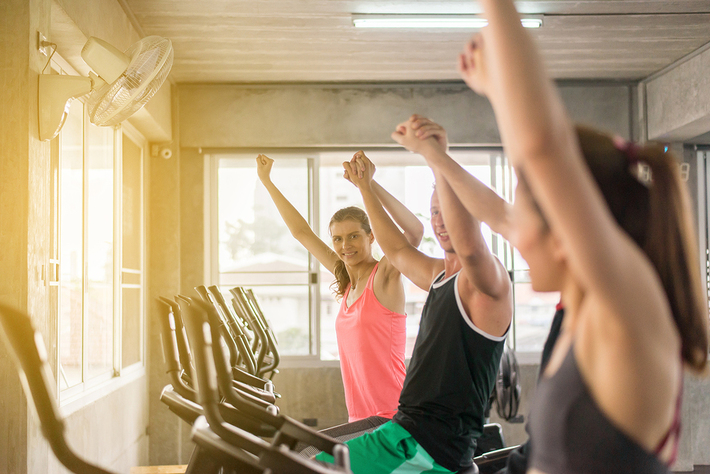 Spin class with three participants raising their hands up.