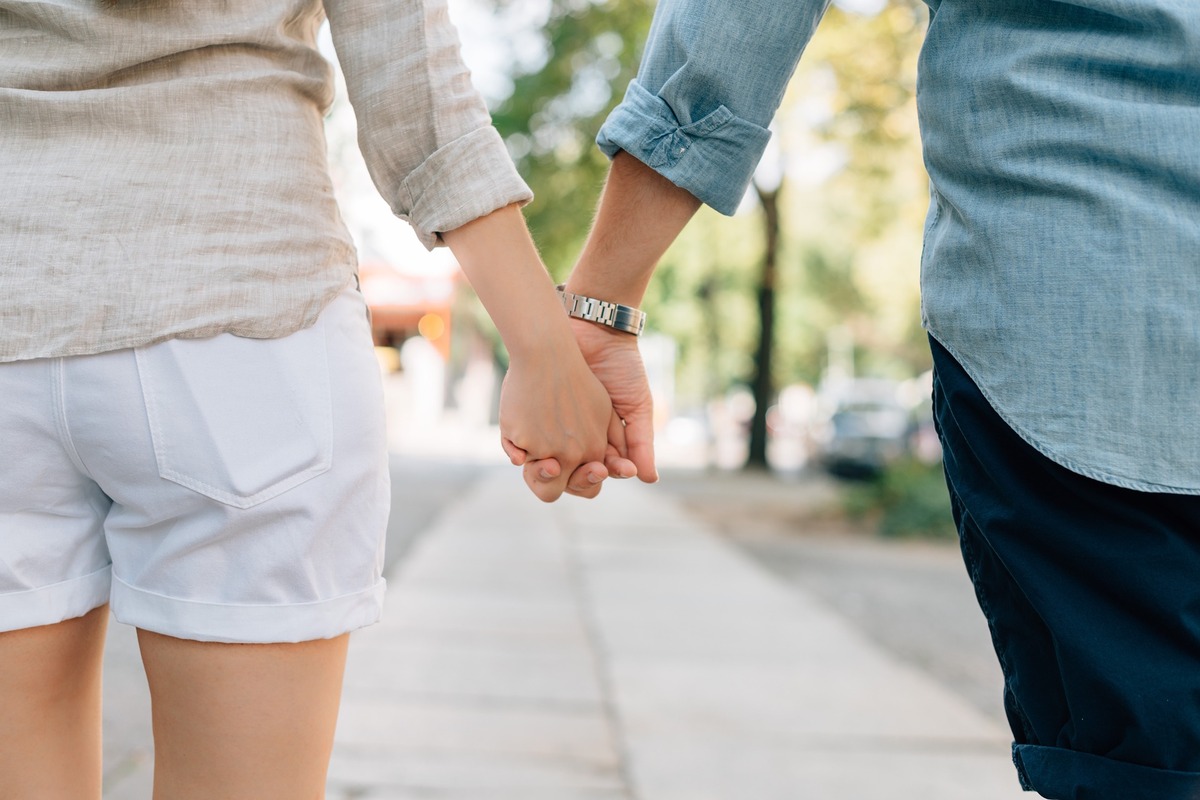 Couple holding hands while walking on a sidewalk.