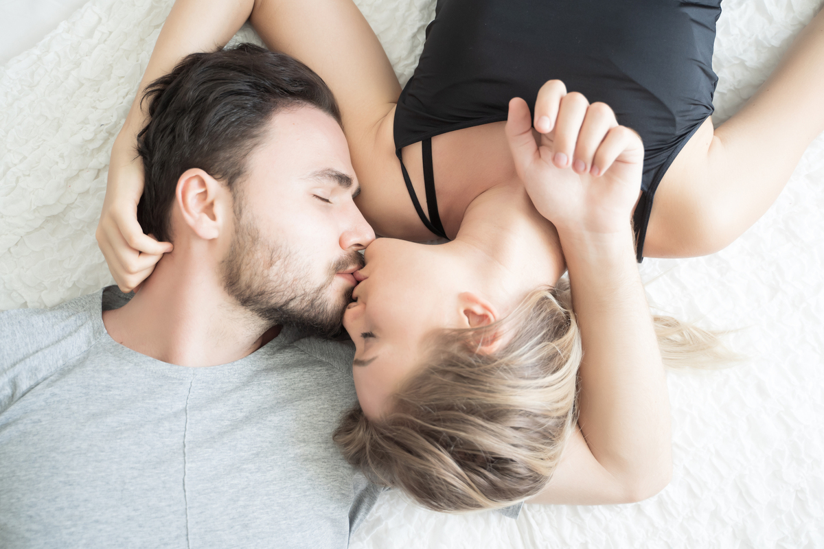Young adult couple lying down kissing.