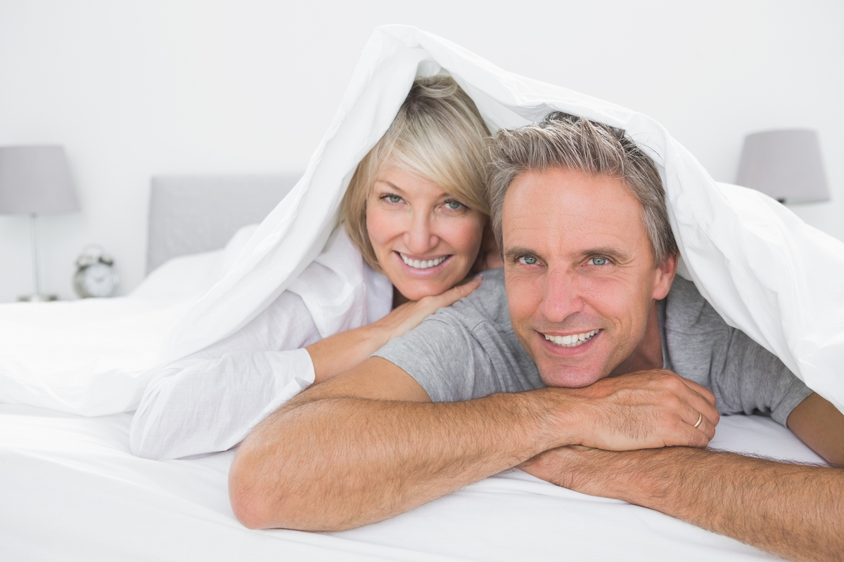 Happy couple lying in a bed with a sheet over their heads.