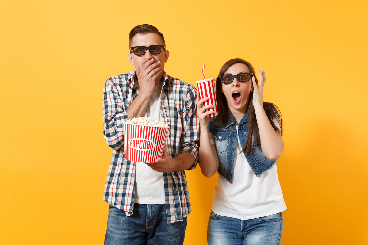Couple looking surprised while wearing 3d glasses and holding popcorn containers.