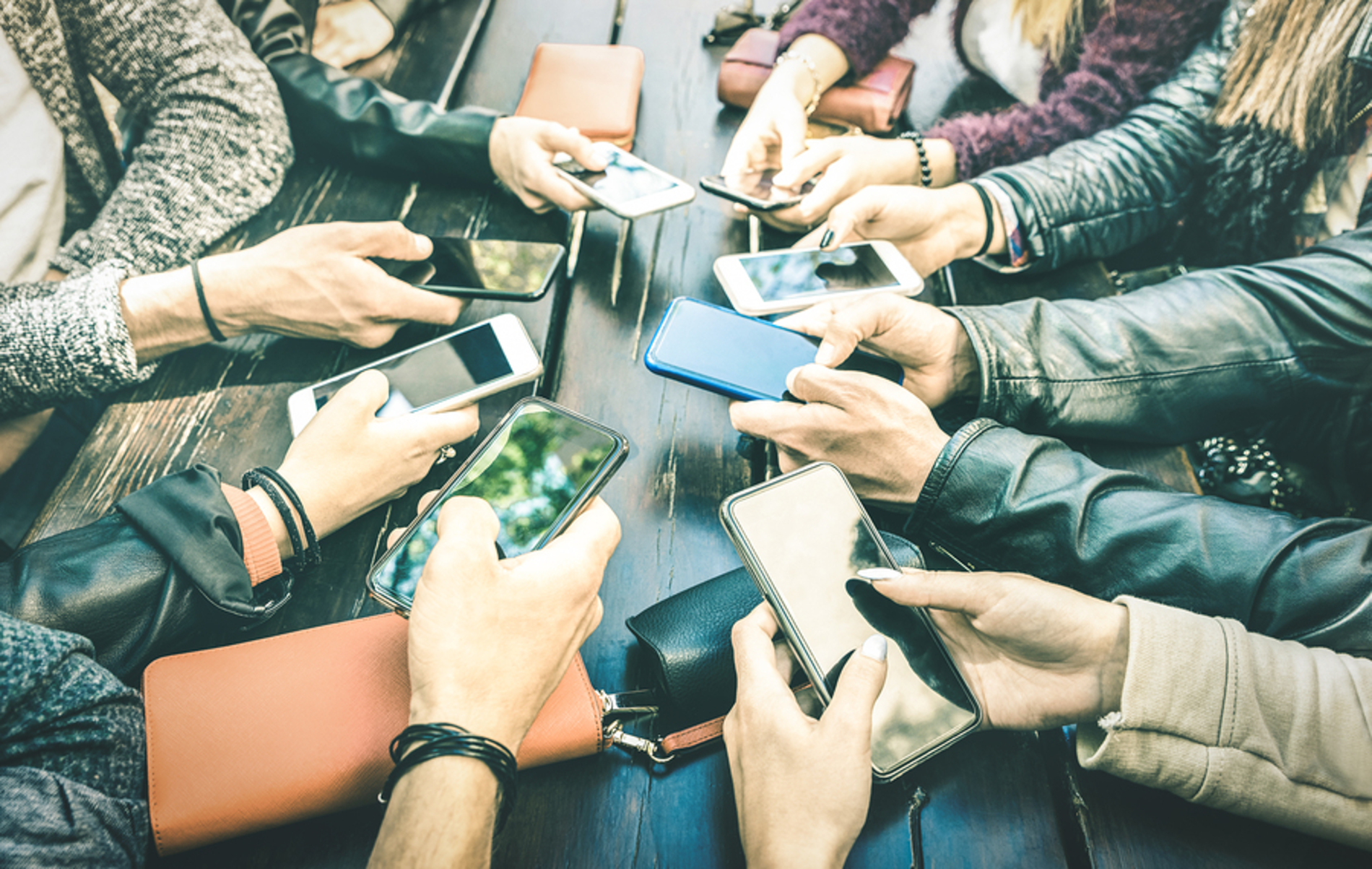 Group of people sitting around a table using their phones.