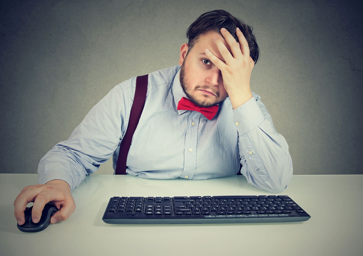 Man using a computer mouse and keyboard and holding his hand on his forehead.