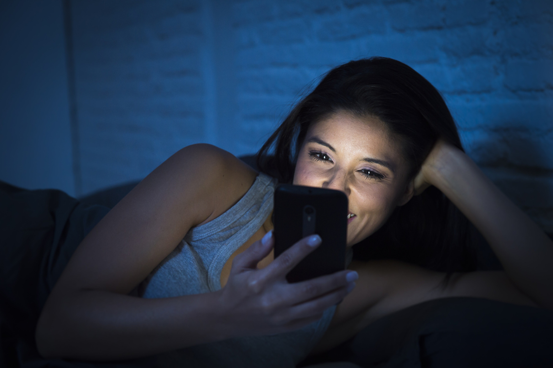 Woman laying in the dark looking at her phone smiling.