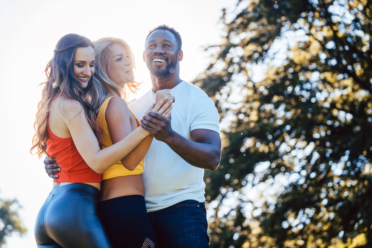 Two women and a man dancing outside.