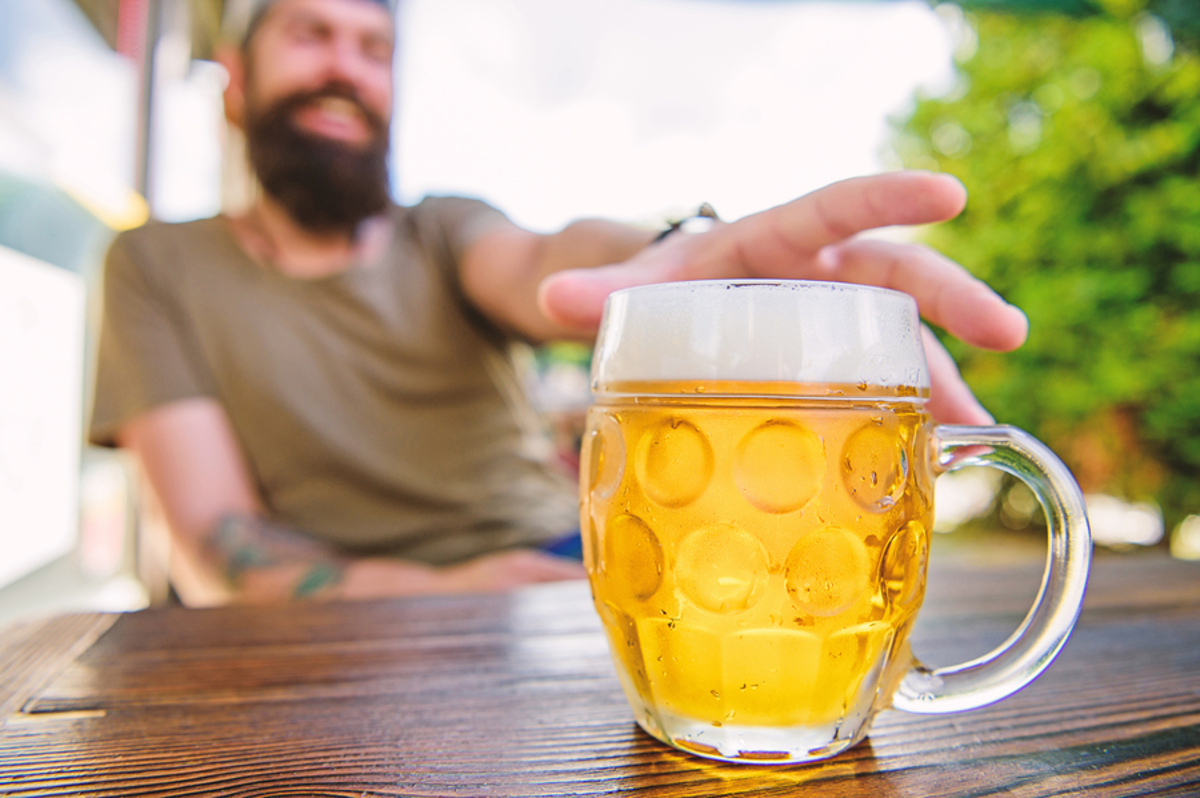 Man sitting down reaching for a mug of beer.