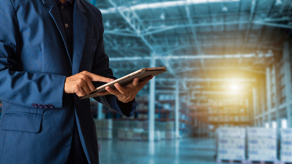 Man in a business suit in a warehouse using his tablet.