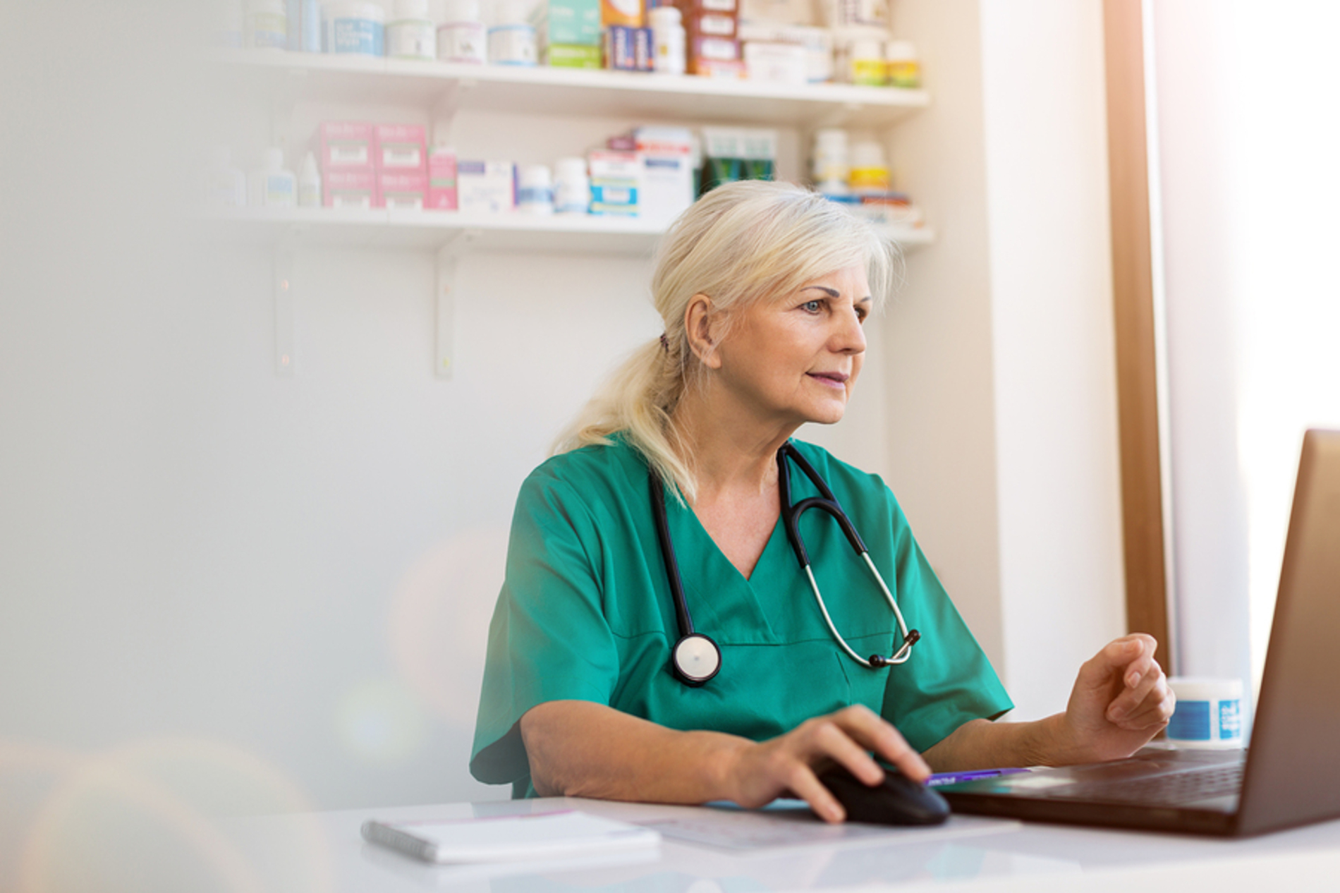 Medical doctor wearing scrubs and a stethoscope looking at a laptop screen.