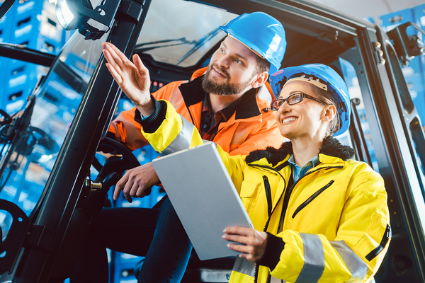 Two construction workers sitting in a heavy machine with hard hats.