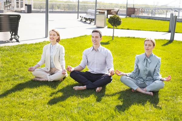 Three people sitting on the grass with legs crossed relaxing.
