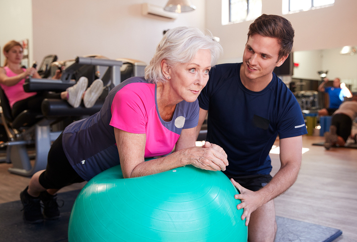 Older woman working out at a gym with a trainer.