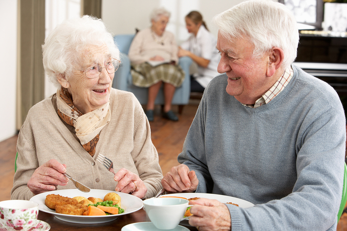 Elderly couple sitting at a table eating dinner.