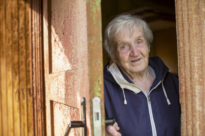 Elderly woman coming outside through a partially open door.