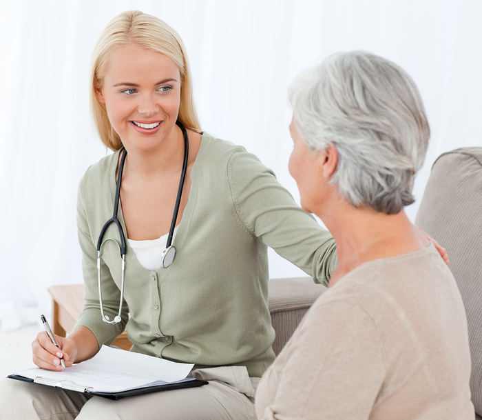 Woman wearing a stethoscope around her neck speaking with an elderly woman.